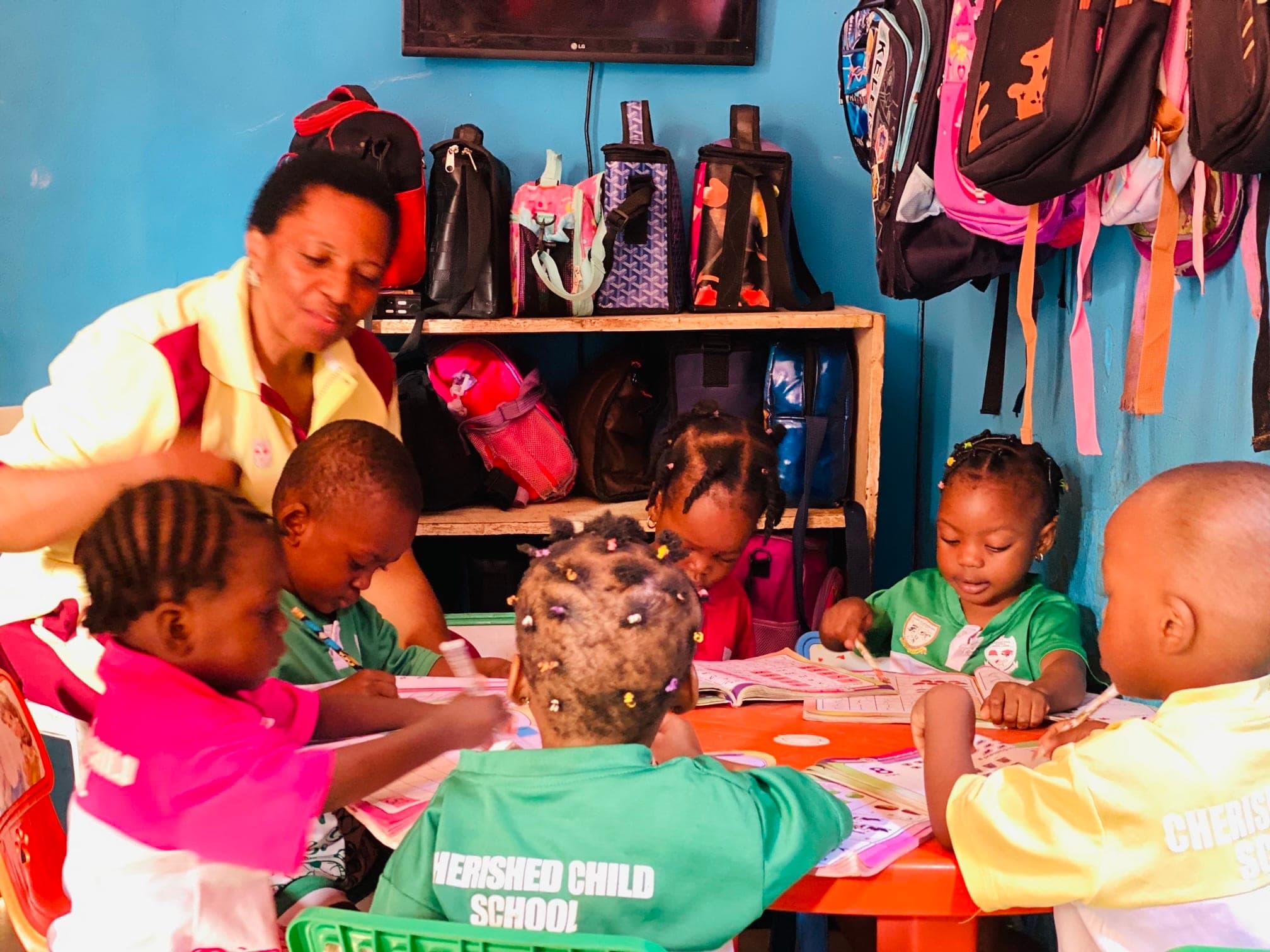 A teacher guiding nursery pupils through written work at a table in a bright classroom